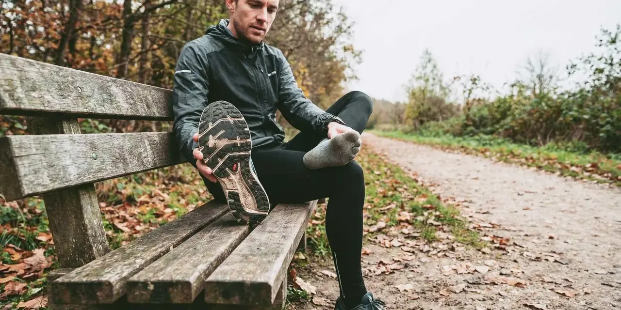 Runner seduto su una panchina controlla le sue scarpe da corsa, pensando a ogni quanto cambiarle per non incorrere in infortuni.