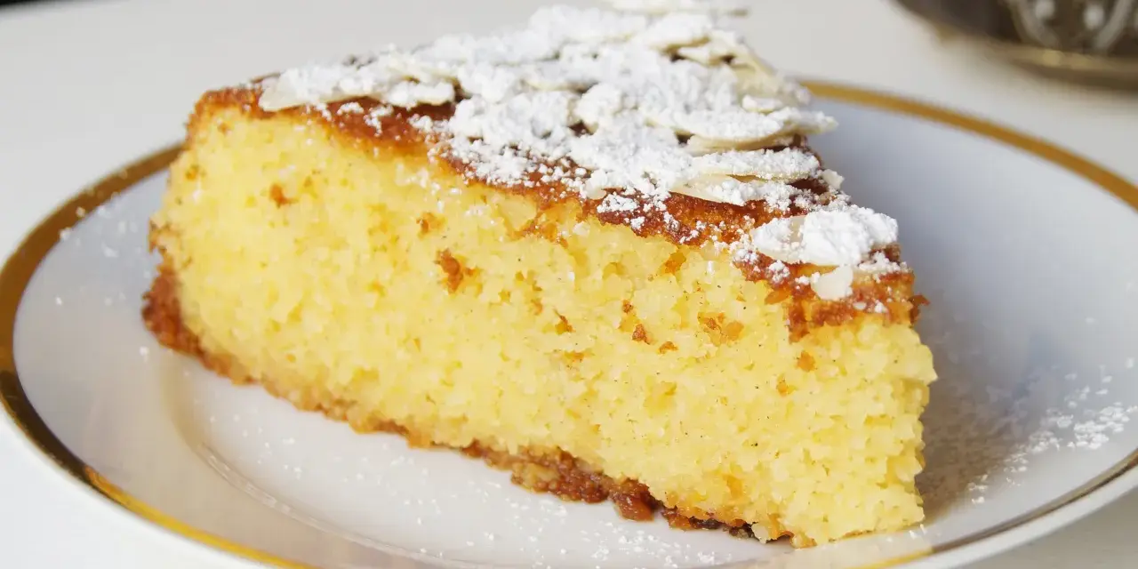 Rebanada de tarta de almendra esponjosa, espolvoreada con azúcar glas y láminas de almendra.