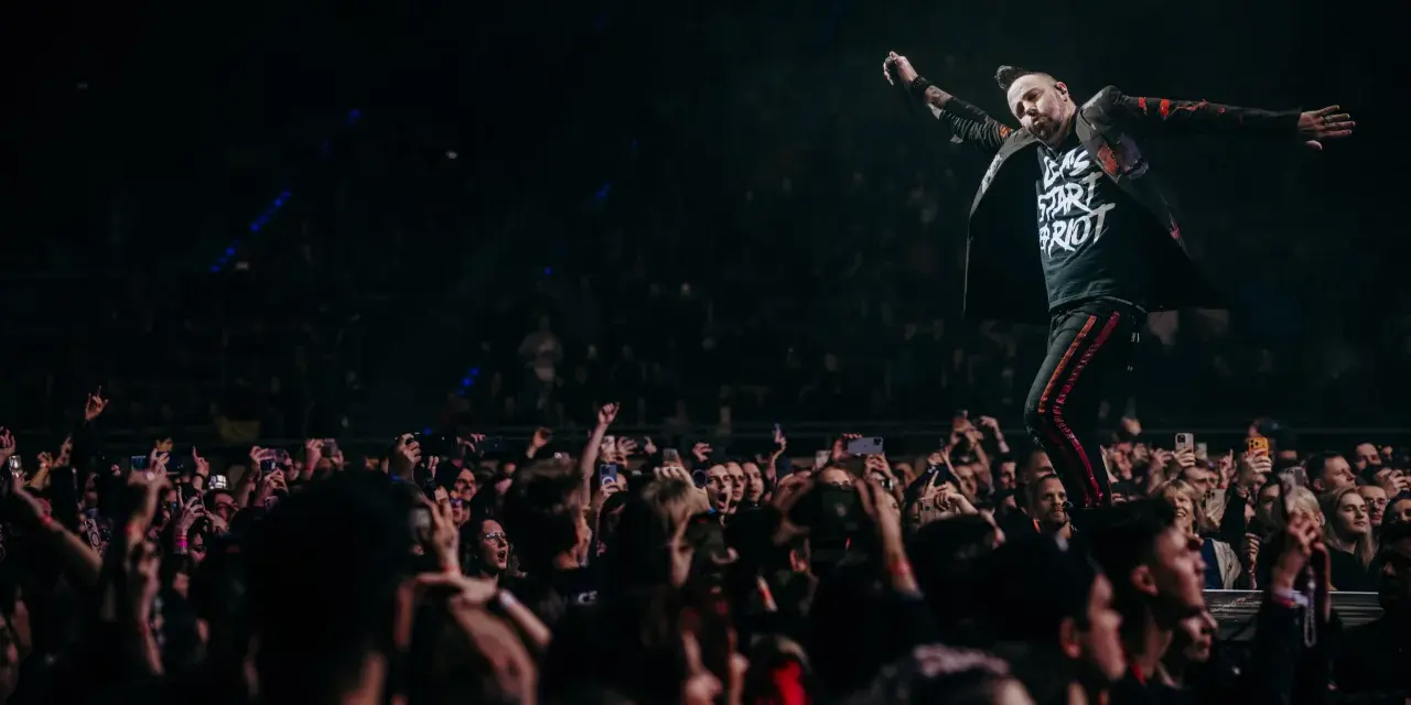 Wokalista Three Days Grace Polska na scenie, z tłumem fanów nagrywających koncert telefonami.