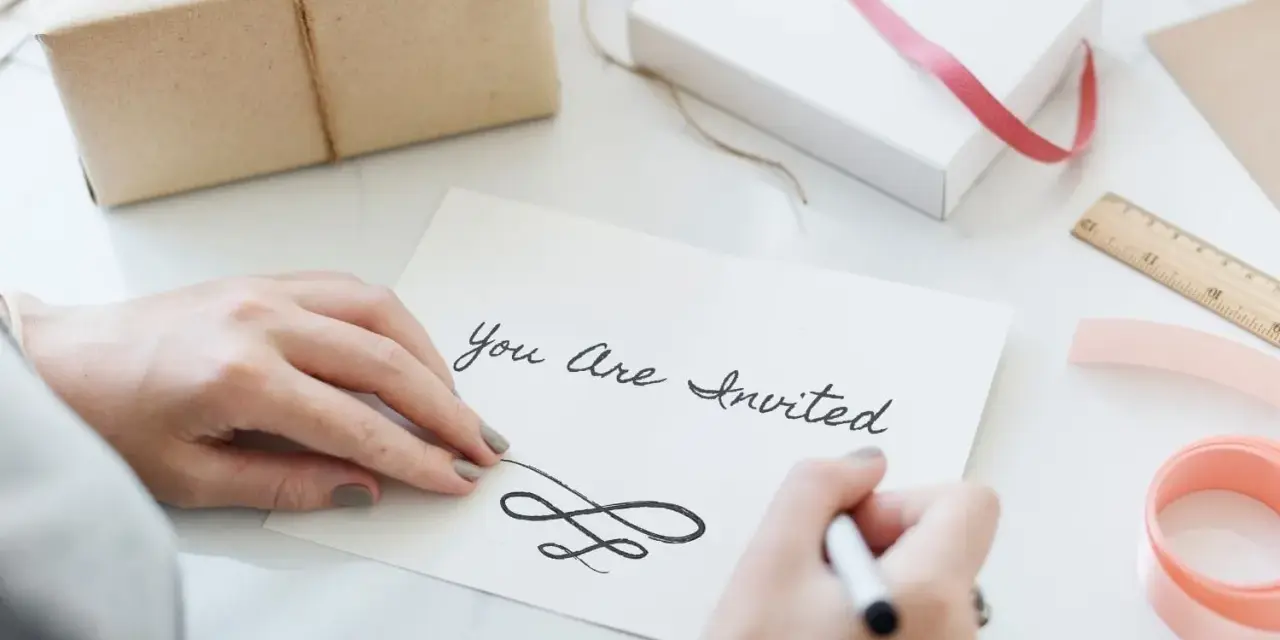 Ręce piszą zaproszenie "You Are Invited". Dowiedz się, jak napisać zaproszenie na urodziny po angielsku.