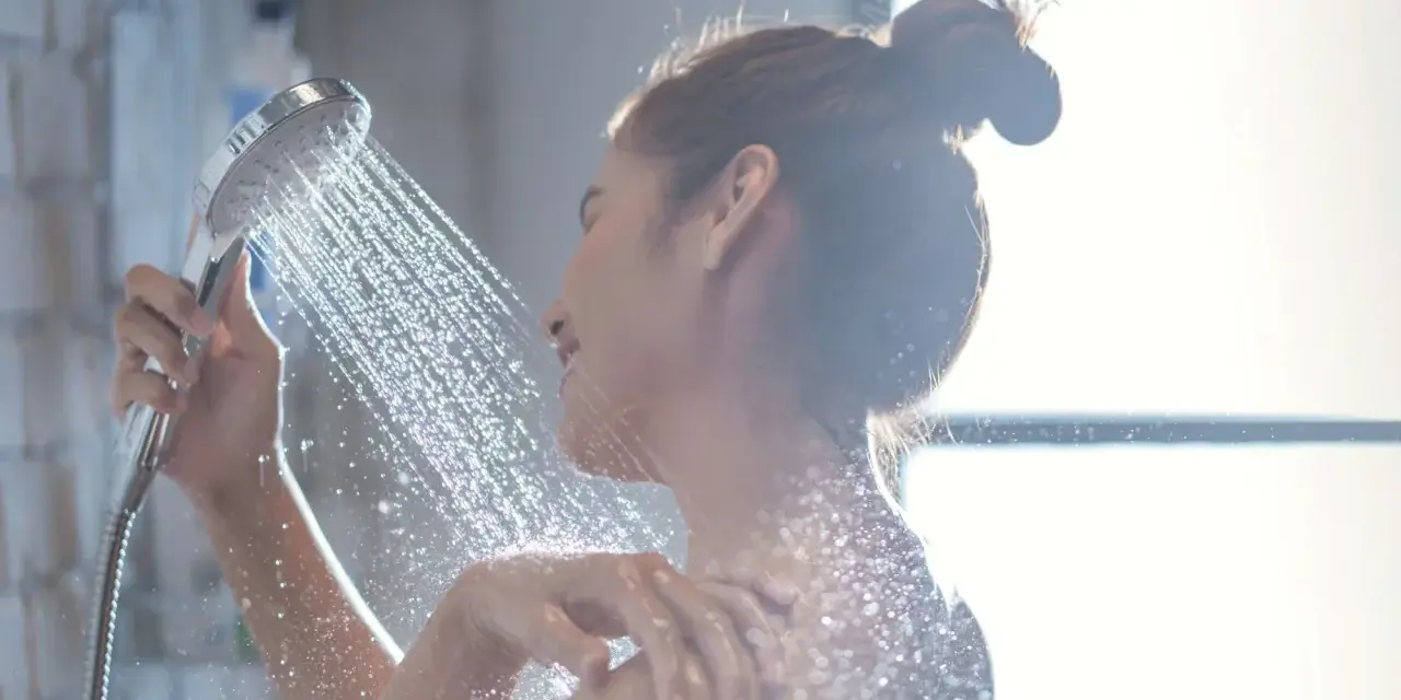 Donna sotto la doccia, l'acqua della doccia esce alternativamente calda e poi fredda, creando un effetto rinfrescante.
