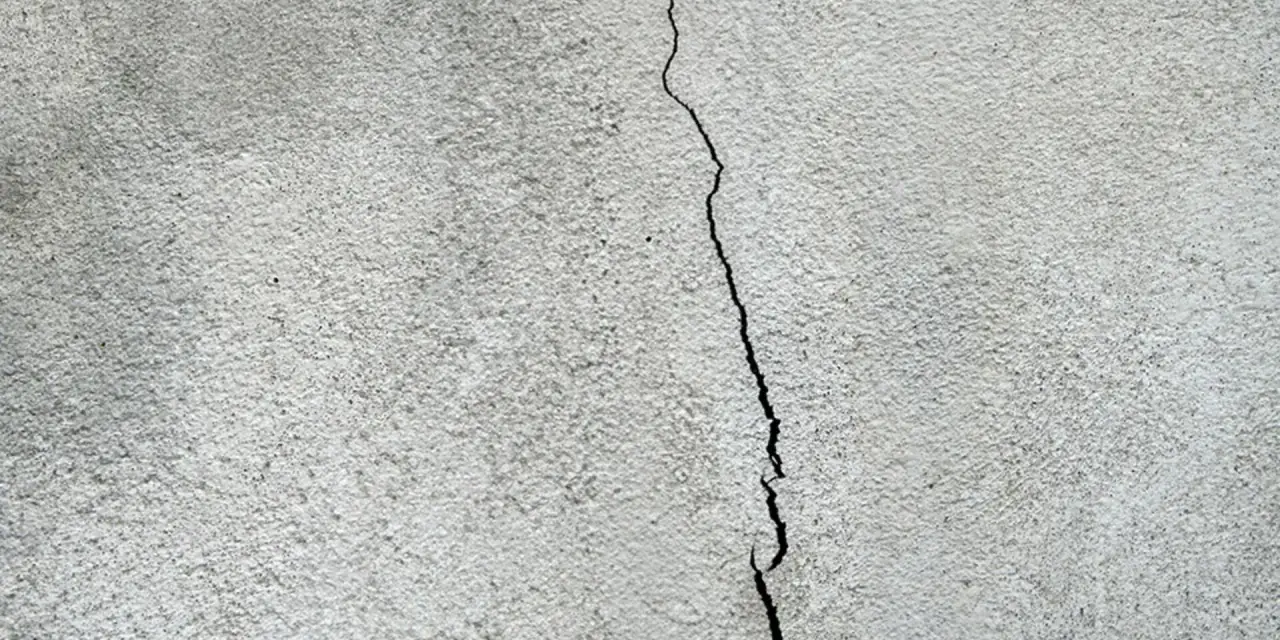 En spricka löper vertikalt över en grov, grå yta, som kan vara en husgrund som behöver putsa.