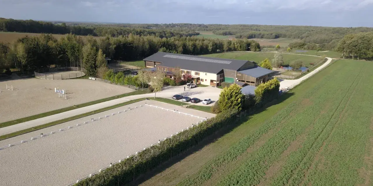 Vue aérienne d'une écurie avec manège et carrière de dressage. Le système de **carrière subirrigation** assure un sol parfait pour les chevaux.
