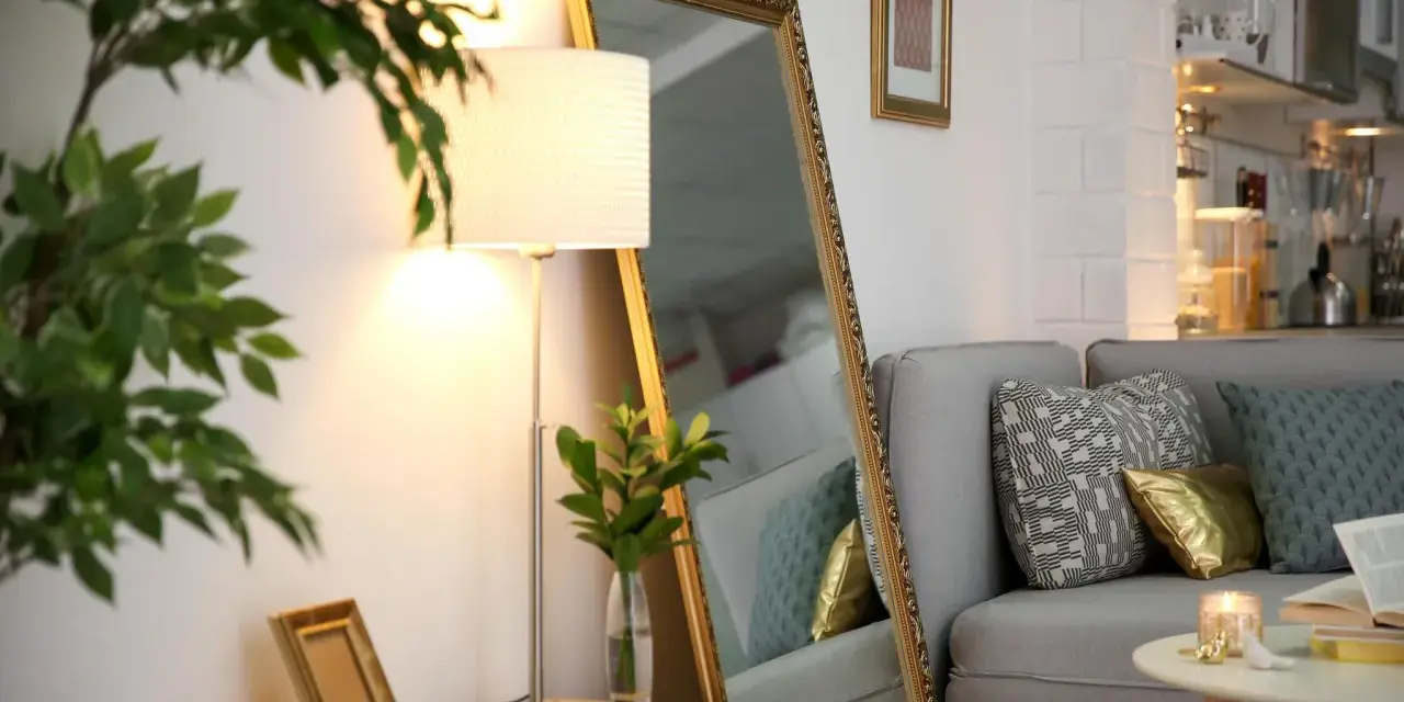 Ein großer Spiegel und eine Stehlampe helfen, die dunkle Wohnung heller zu machen. Ein Sofa mit Kissen und ein kleiner Tisch vervollständigen die Szene.