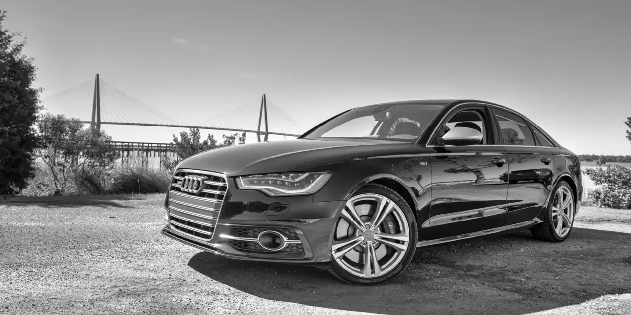 Elegancki czarny Audi S6 C7 z charakterystycznym grillem i felgami, zaparkowany na tle mostu wiszącego.