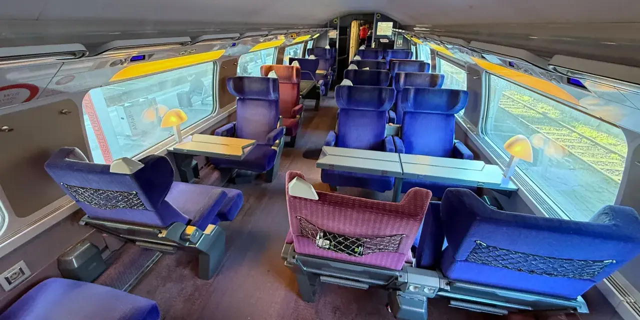 Interior of a bullet train, ready for a journey from Paris to Nice. Plush blue seats with tray tables line the carriage.
