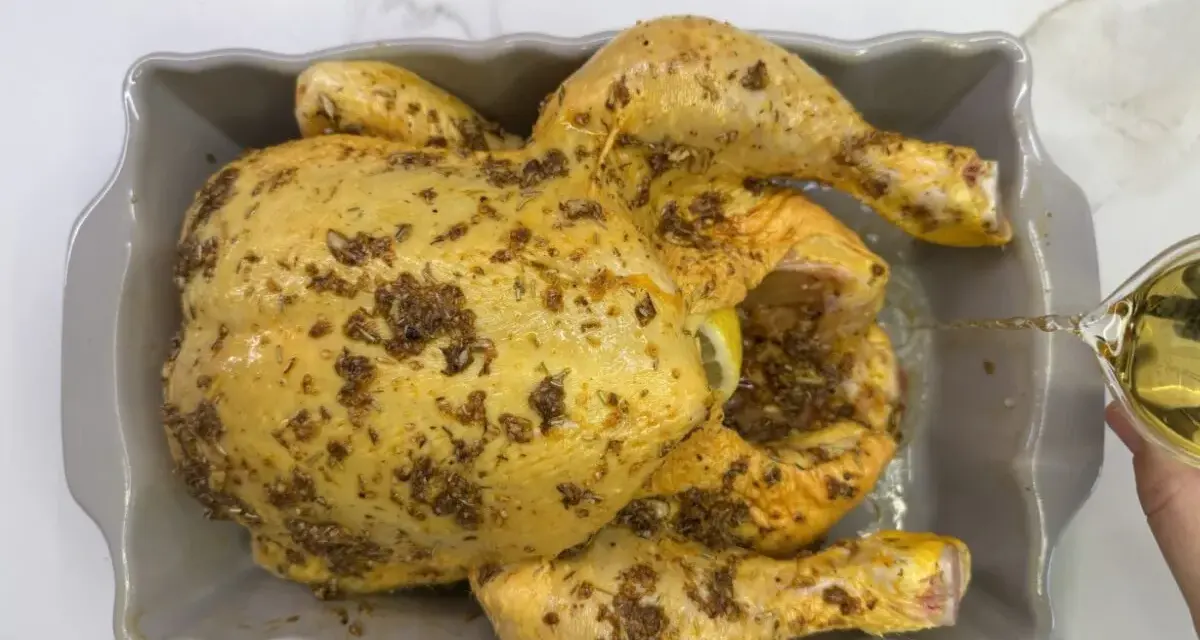 Un pollo al ast, sazonado y listo para hornear, recibe un chorrito de aceite para una cocción perfecta.