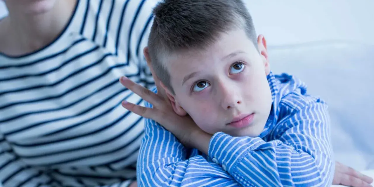 Bambino con sguardo pensieroso, forse durante un test autismo bambini 2 anni. La madre lo osserva con preoccupazione.