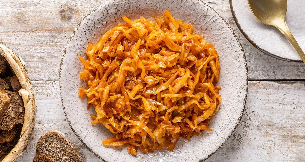 Un saporito cappuccio stufato in padella, servito in un piatto rustico, accompagnato da pane scuro e una posata dorata.