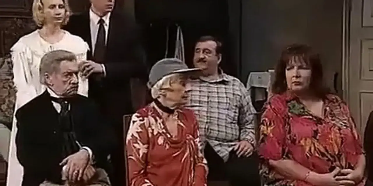 Scena z filmu "Tango" Mrożka. Grupa osób siedzi i stoi w pomieszczeniu.