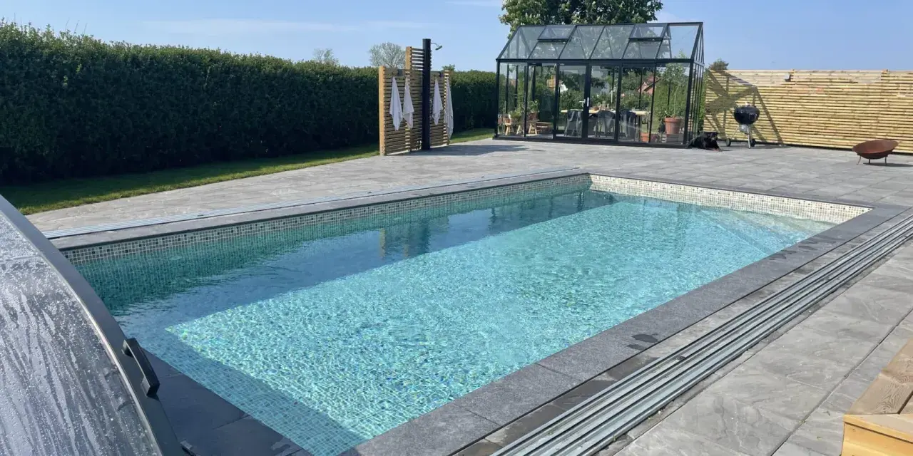 En vacker pool med mosaikdetaljer, perfekt för att bygga egen pool. Omgiven av en modern uteplats med växthus och dusch.