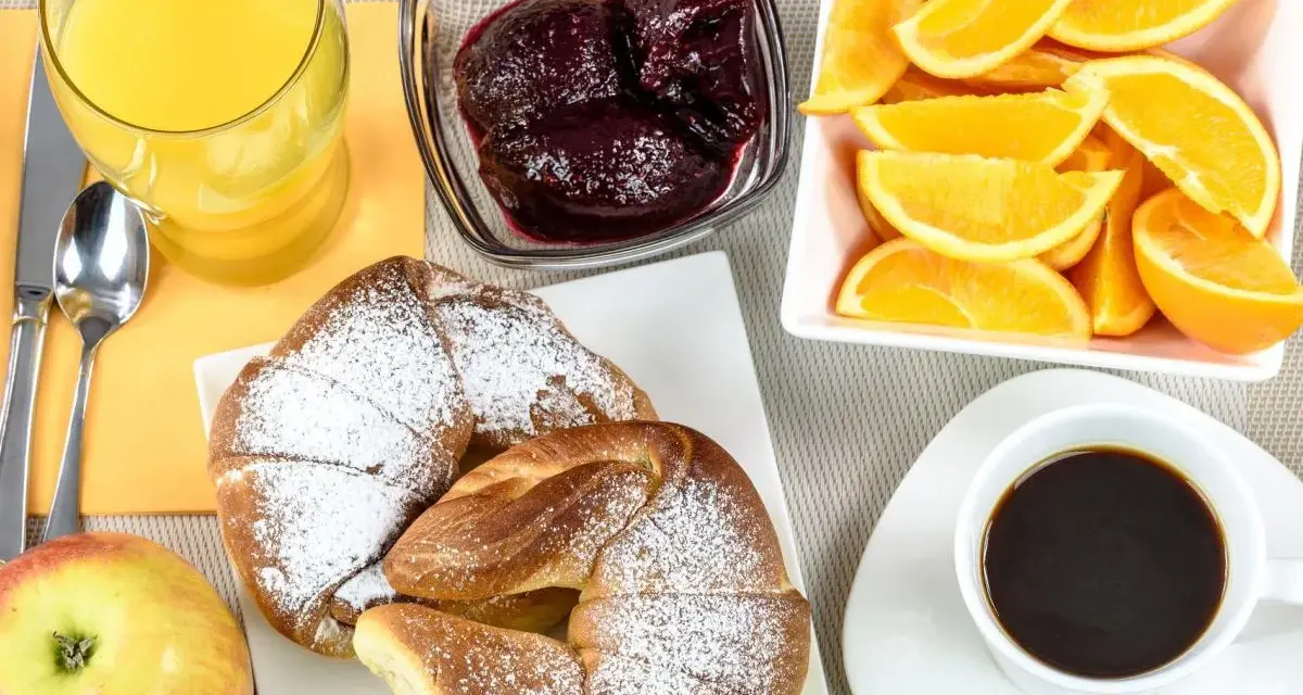 Pyszne śniadanie kontynentalne: rogaliki z cukrem pudrem, pomarańcze, dżem, sok i kawa.