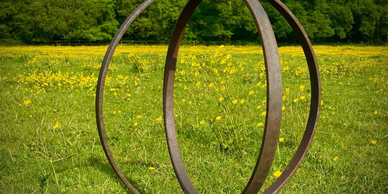 Metallskulptur im Feld mit gelben Blumen. Eine Idee, wie man ein Rondell im Garten gestalten kann, mit rustikalem Charme.