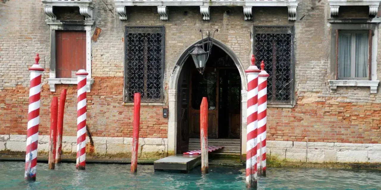 I pali di Venezia, chiamati bricole, segnano il canale davanti a un palazzo storico.