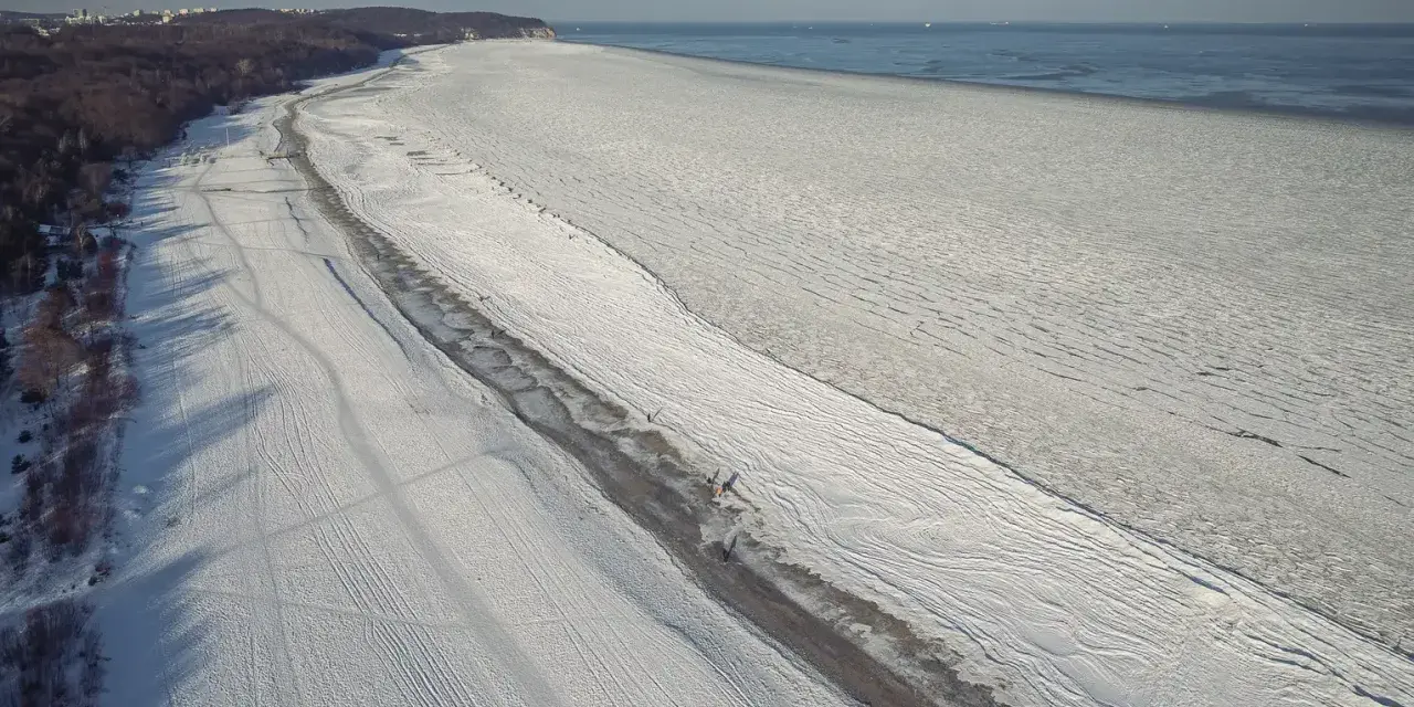 Zamarznięta plaża i Bałtyk, jakby czas się zatrzymał od kiedy powstało morze bałtyckie. W oddali widać statki.