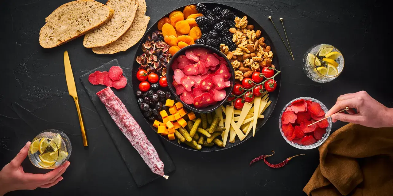 Planche apéro généreuse : charcuterie, fruits secs, olives, tomates, fromage, cornichons et pain. Une belle idée pour un moment convivial.