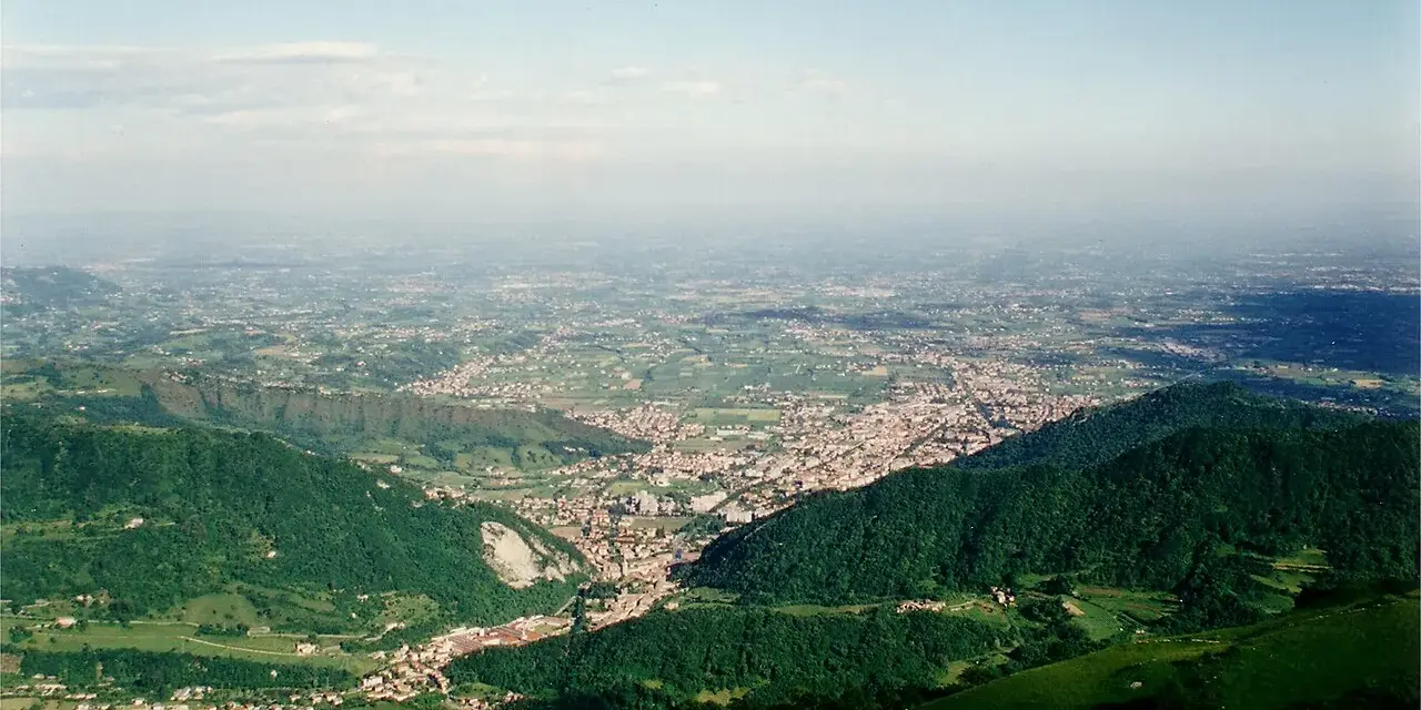 Vista panoramica dalla sella di Fadalto su una vasta pianura punteggiata di case e campi, con colline verdi in primo piano.
