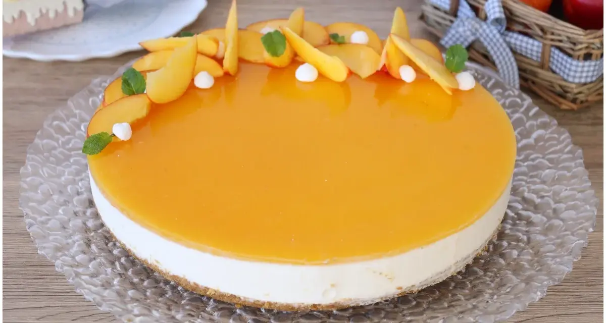 Delizioso cheesecake alle pesche con glassa lucida e fette di pesca fresca, guarnito con menta e piccole meringhe.