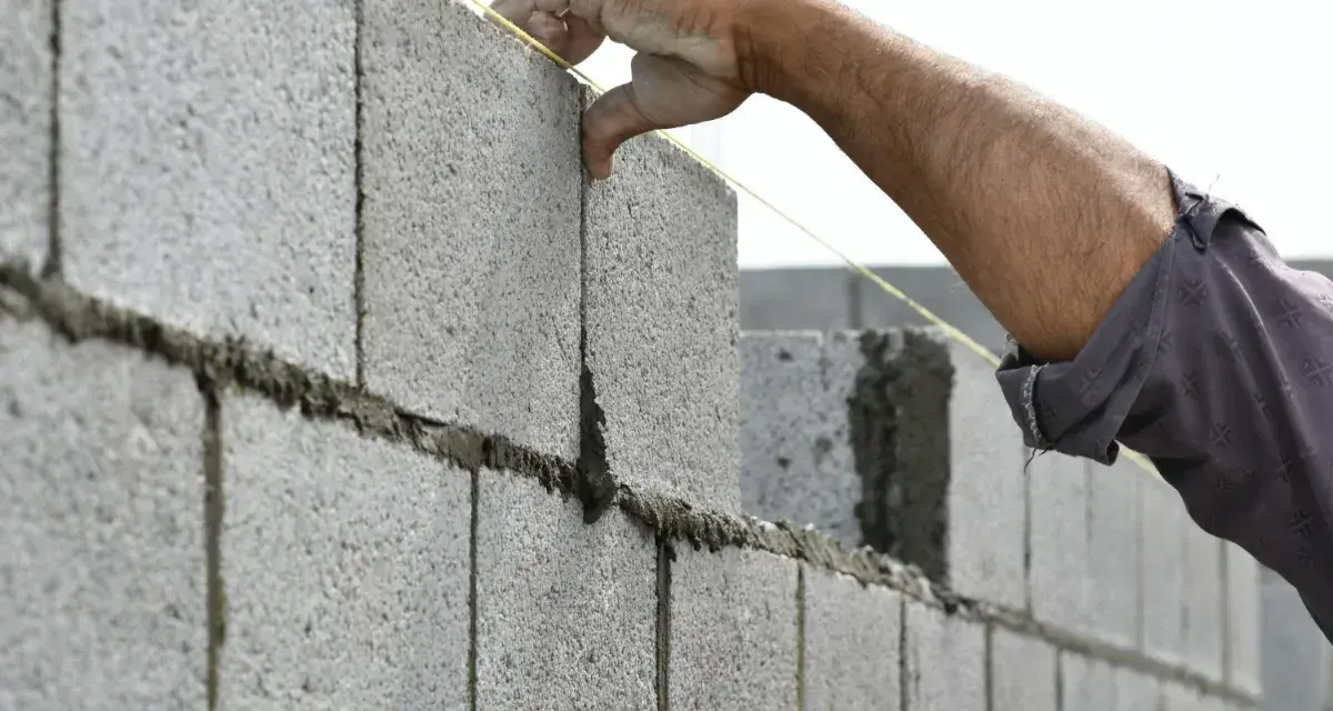 Pose d'un parpaing pour un mur de 25m. Le maçon ajuste la brique avec précision.