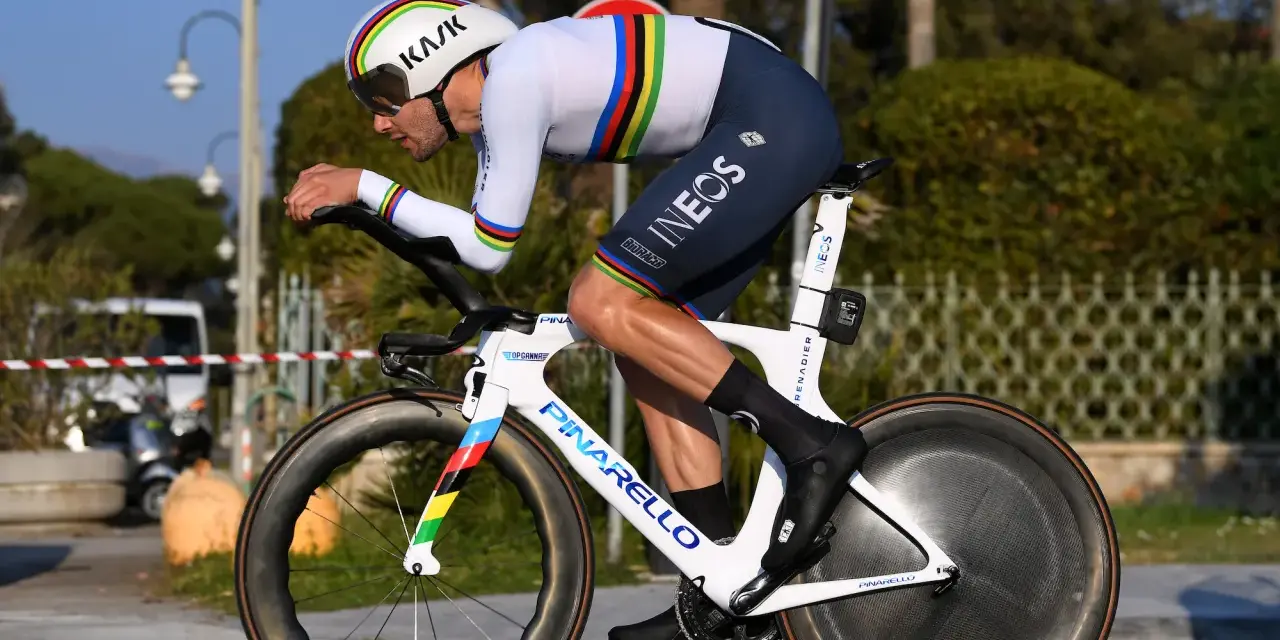A cyclist in a rainbow jersey races a time trial bike, pushing hard during the Tour de France.