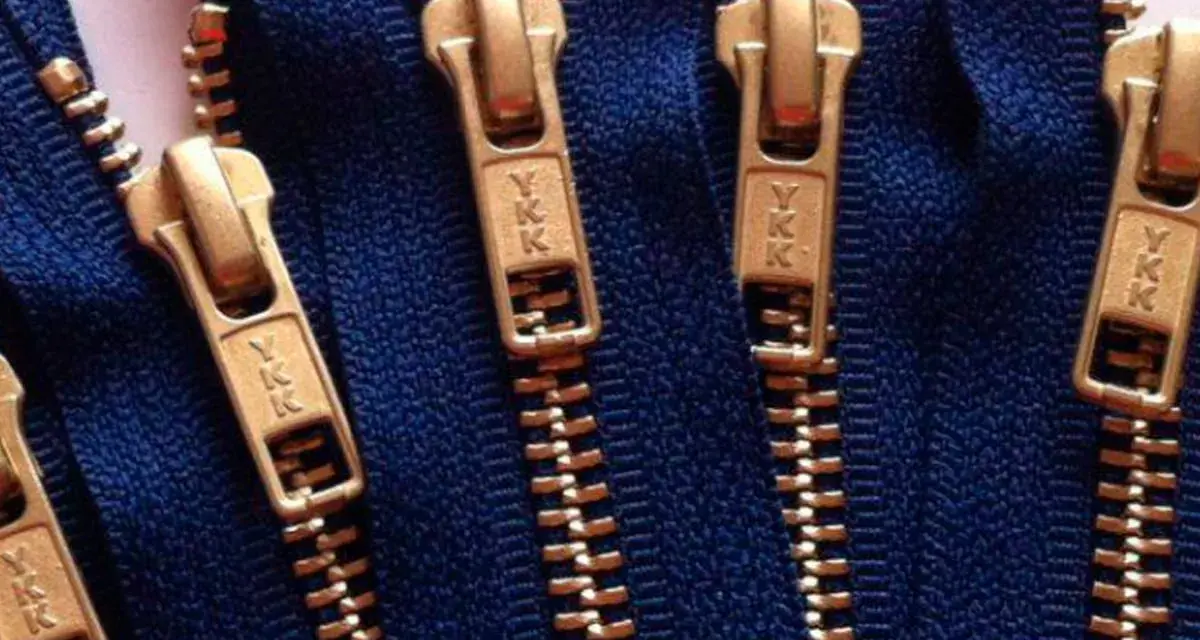 Primer plano de varias partes de una cremallera YKK dorada sobre tela azul.