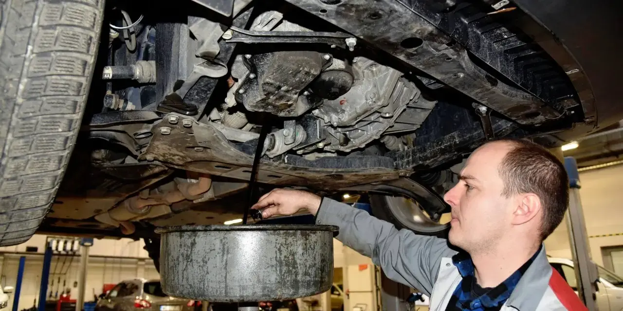 Mechanik spuszcza olej z silnika samochodu. Regularna wymiana oleju to klucz do długowieczności auta.