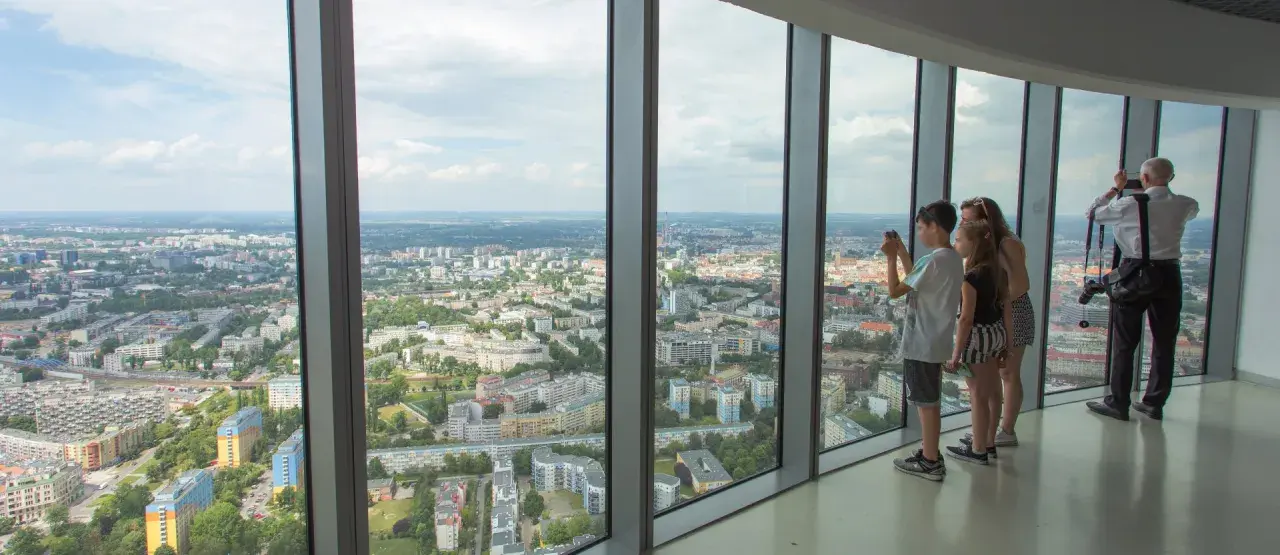 Widok z tarasu widokowego Sky Tower. Rodzina podziwia panoramę miasta, doceniając jego ogromną wysokość.