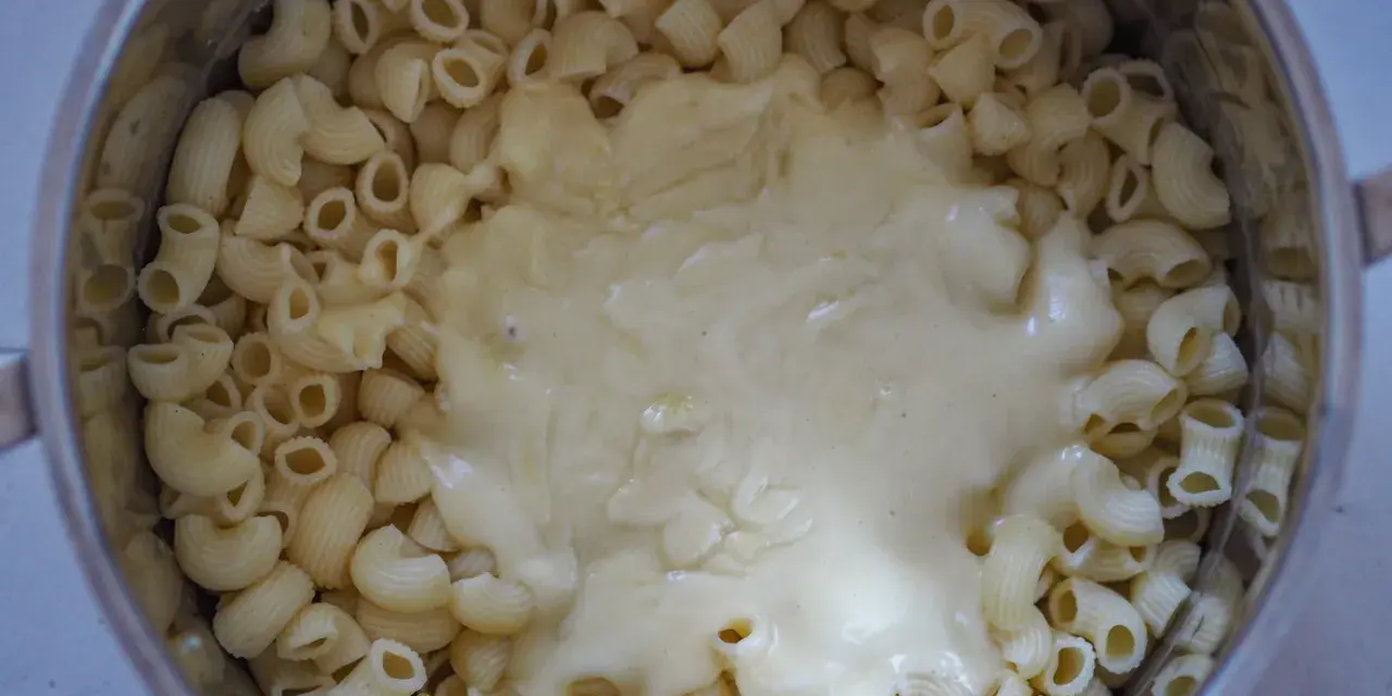 Gęsty, kremowy sos serowy otula makaron w garnku, tworząc pyszny makaron mac and cheese.