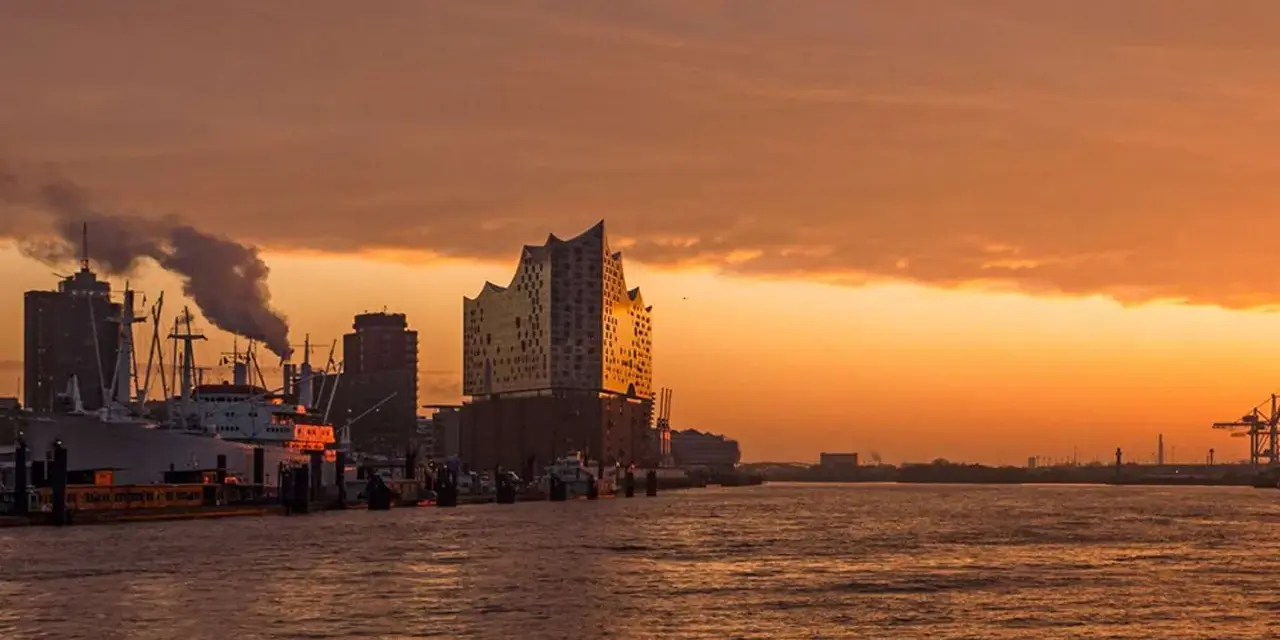 Coucher de soleil sur le port de Hambourg, idéal pour visiter Hambourg en 3 jours. Bateaux, grues et la Philharmonie de l'Elbe se reflètent sur l'eau.