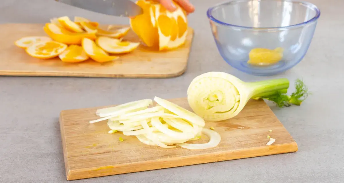 Frischer Fenchelsalat wird zubereitet. Eine Person schneidet Orangen, während Fenchelscheiben auf einem Holzbrett liegen.