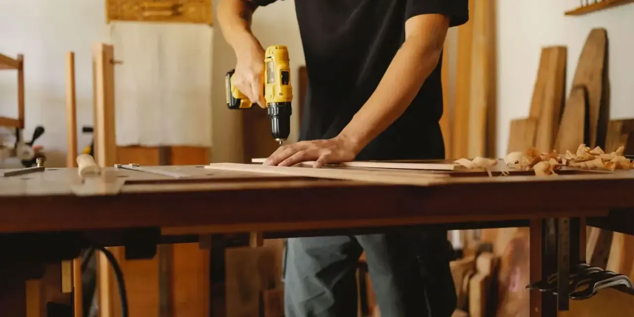 Mann bohrt Holzbretter, um seine Werkstatt einzurichten. Hobelspäne liegen auf dem Tisch.