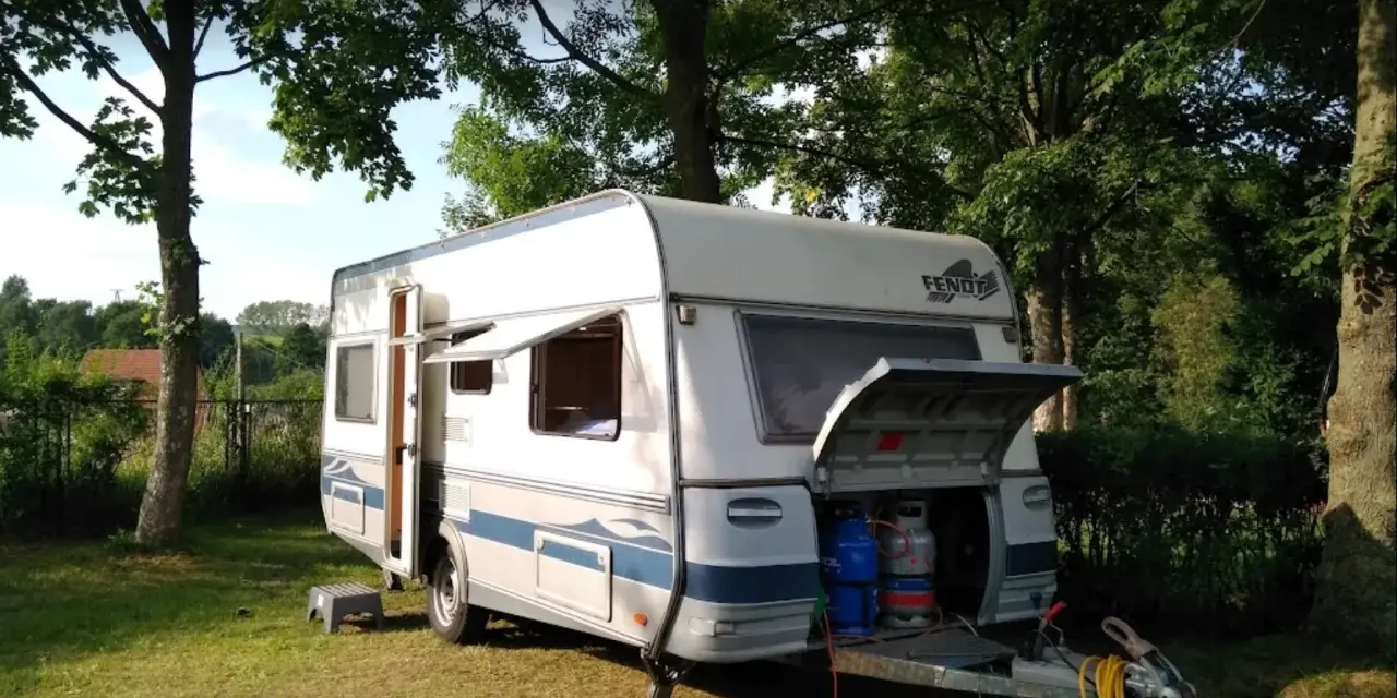 Przygotowania do wypoczynku na **camping Duszniki Zdrój**. Przyczepa kempingowa z otwartym bagażnikiem, w którym widać butle gazowe.