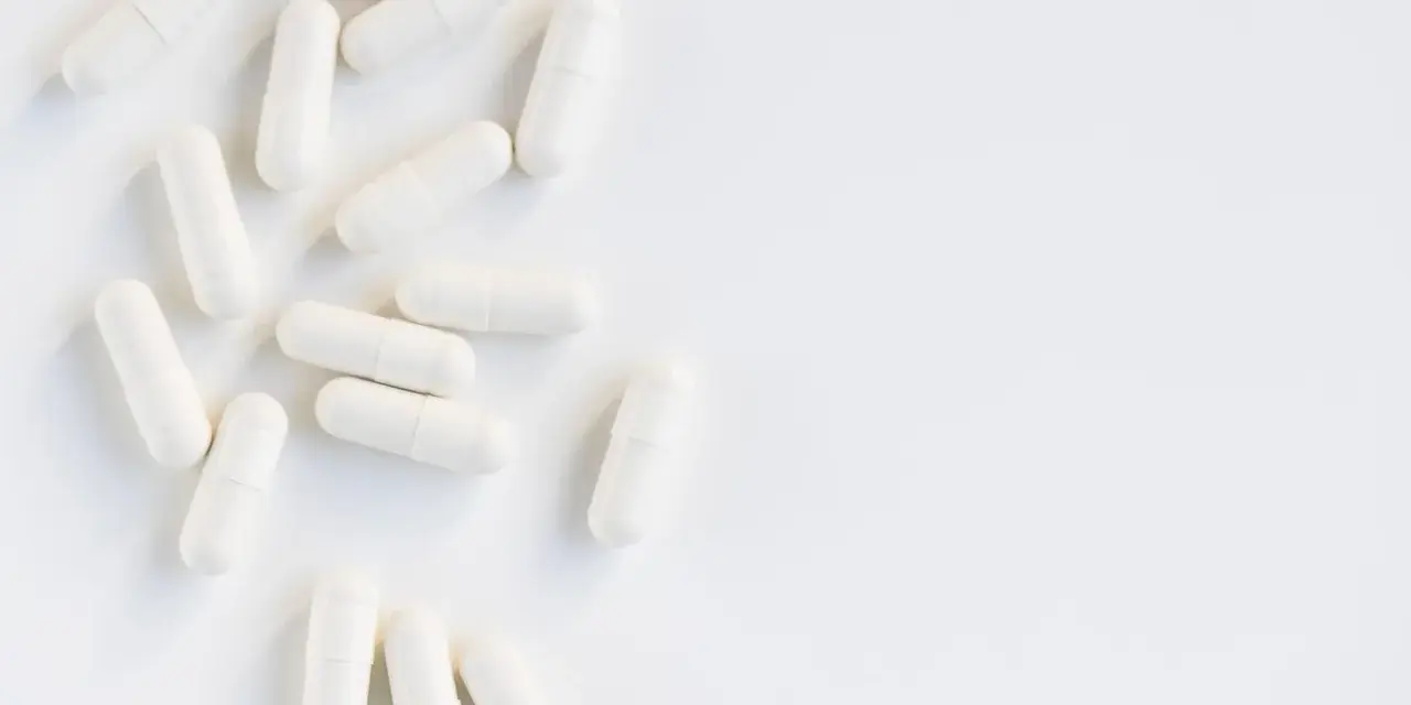 Vita kapslar utspridda på en vit yta. Kan dessa orsaka l-glutamin biverkningar?