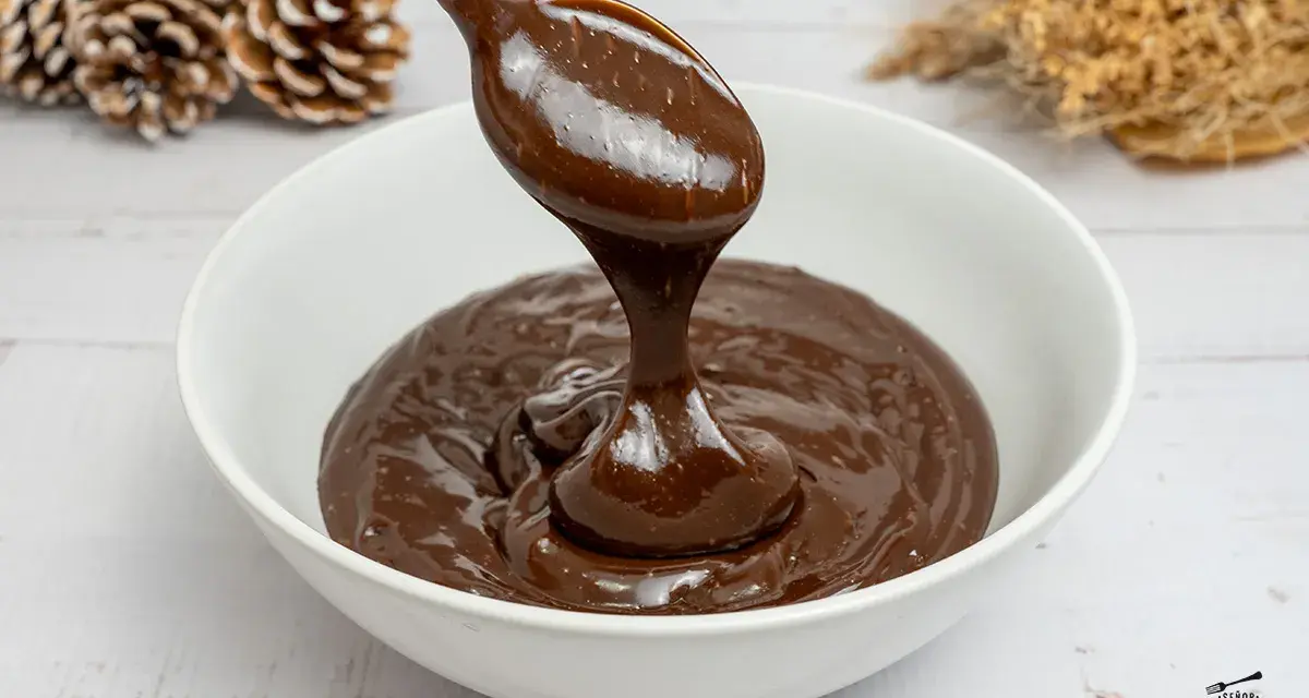 Cuchara con ganache de chocolate cayendo en un cuenco blanco. El chocolate es brillante y sedoso, perfecto para postres.
