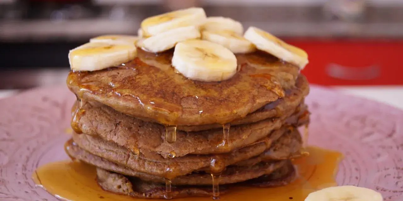 Pila de tortitas de avena y plátano, cubiertas con rodajas de plátano y sirope dorado. ¡Un desayuno delicioso!