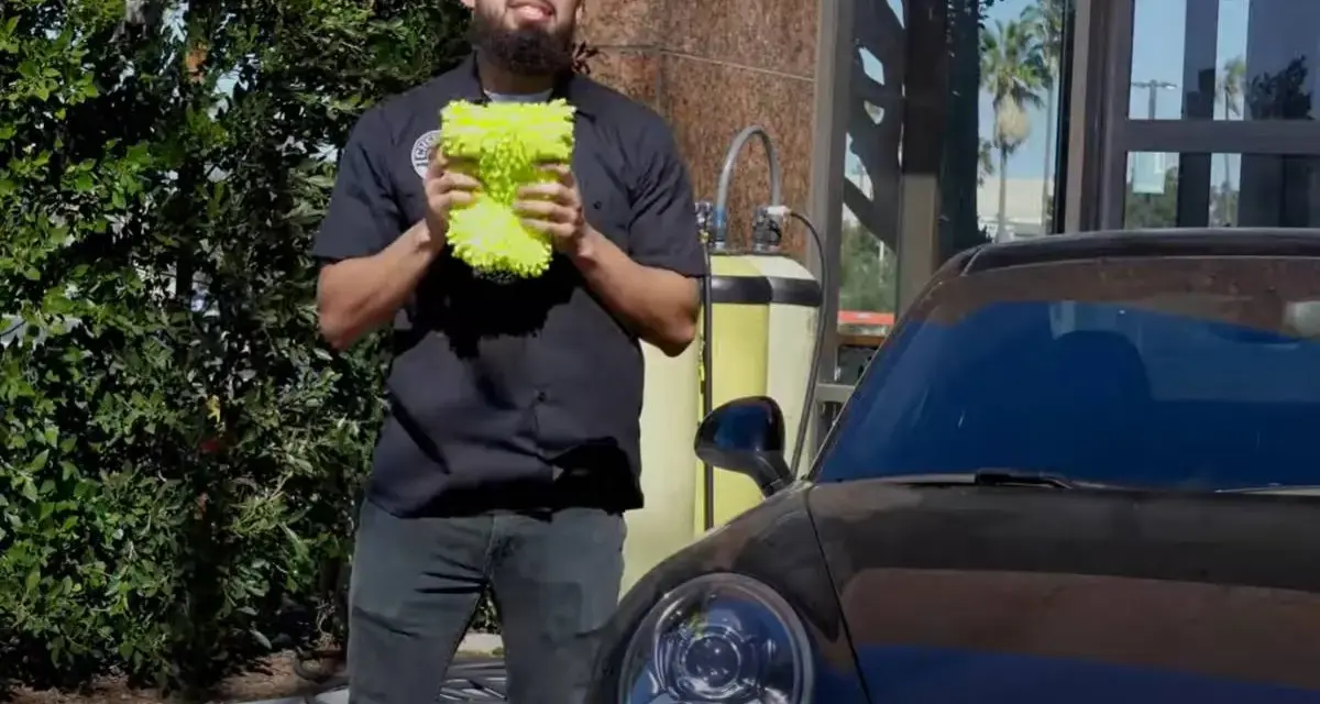 Man holding a fluffy wash mitt, ready to demonstrate how to wash a convertible car.