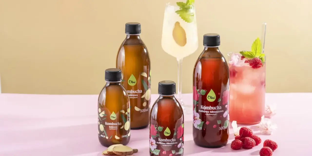 Kombucha co to? Butelki z napojem, malinowo-hibiskusowa i imbirowa, obok drinków z malinami i imbirem.