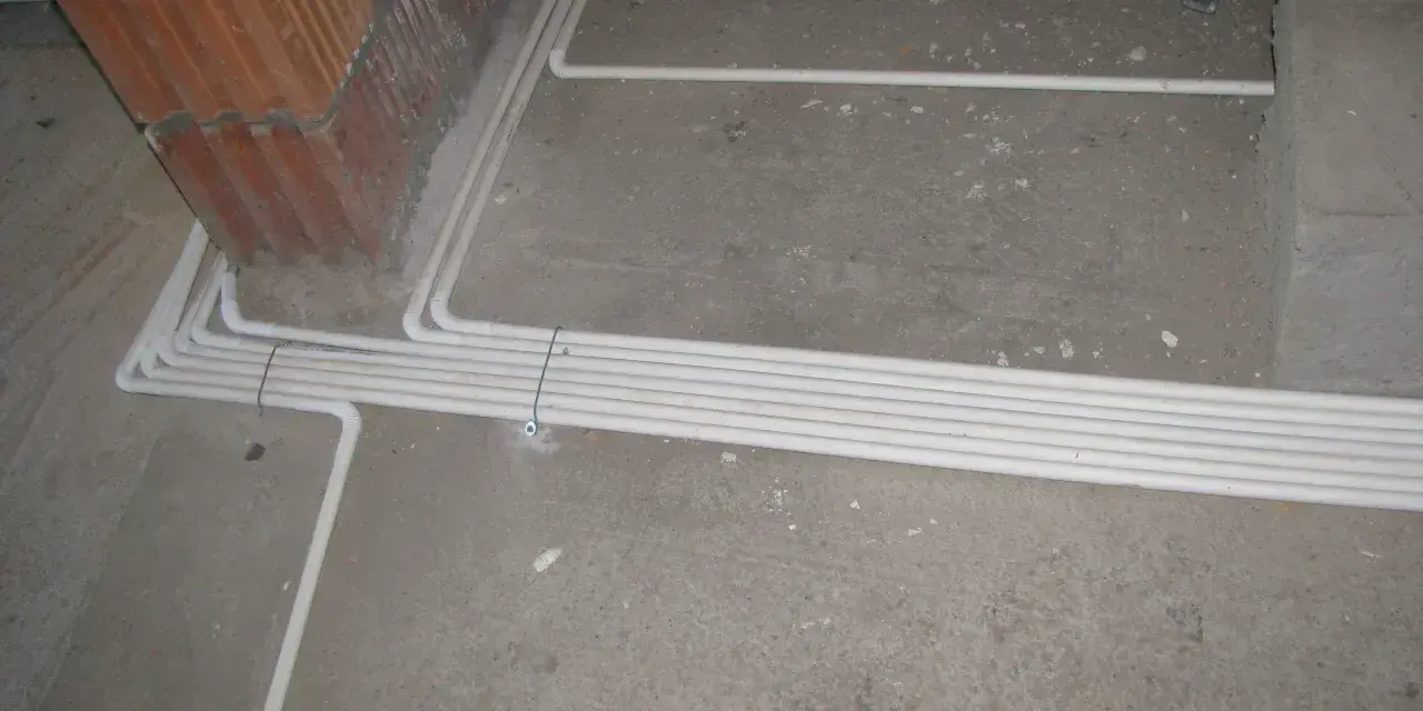 Uporządkowana instalacja elektryczna w podłodze, biegnąca wzdłuż ściany z cegły.