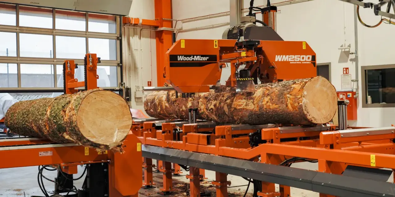 Pomarańczowa maszyna do obróbki drewna Wood-Mizer WM2500 przetwarza pień drzewa na deski.
