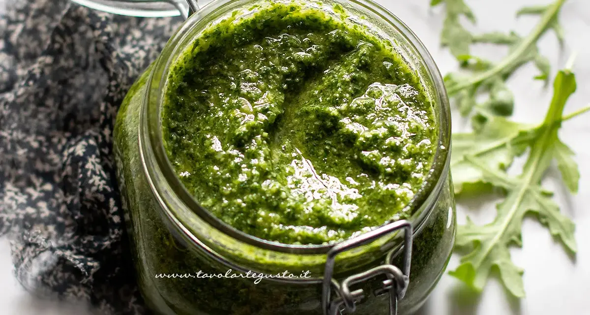 Un vasetto di pesto di rucola fatto in casa, con foglie di rucola fresca sullo sfondo.