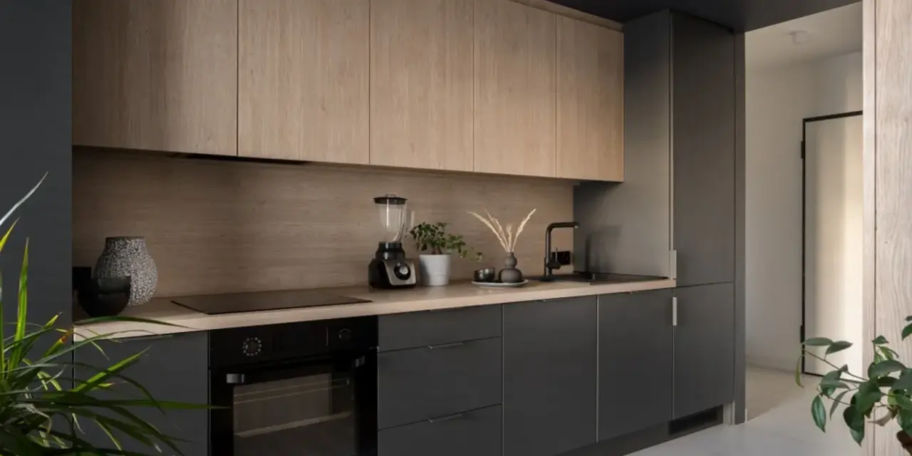 Cocinas de leña modernas con gabinetes de madera clara y encimeras oscuras. Un horno, licuadora y plantas decoran el espacio.