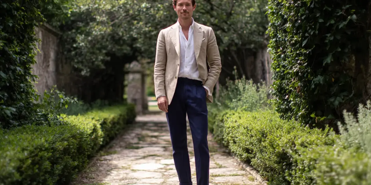 Uomo con giacca beige e pantaloni blu, un look che evoca un raffinato stile francese.