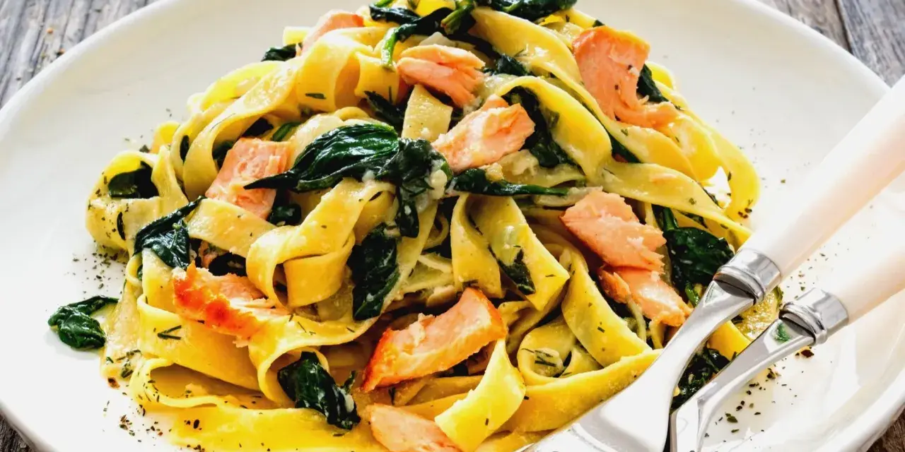 Pyszny makaron z łososiem i szpinakiem, podany na białym talerzu, z widelcem i nożem.