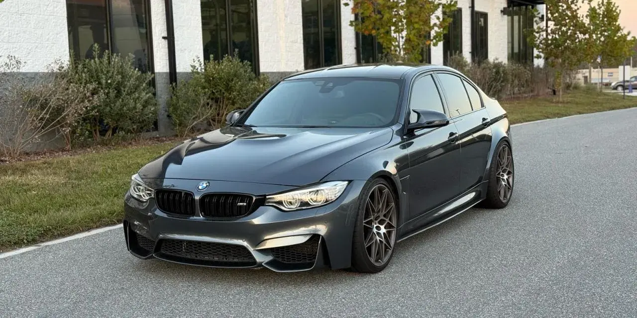 Szary sedan BMW M3 na tle nowoczesnego budynku. Sprawdź aktualną bmw m3 cena i możliwości tego sportowego auta.