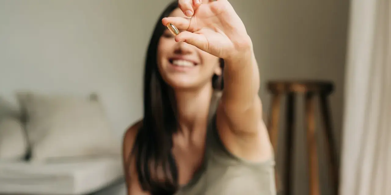 Une jeune femme souriante tient une capsule, symbole d'une cure de vitamine pour un bien-être quotidien.