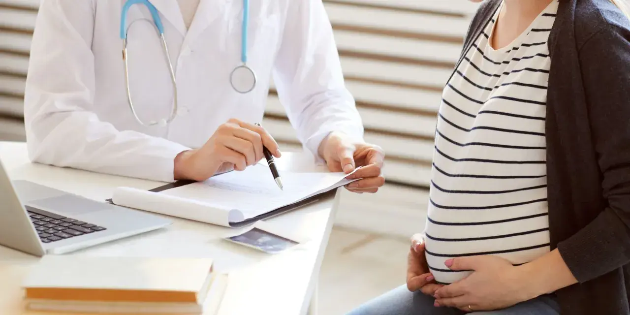 Lekarz omawia z ciężarną pacjentką kolejne trymestry ciąży, notując coś na dokumentach.
