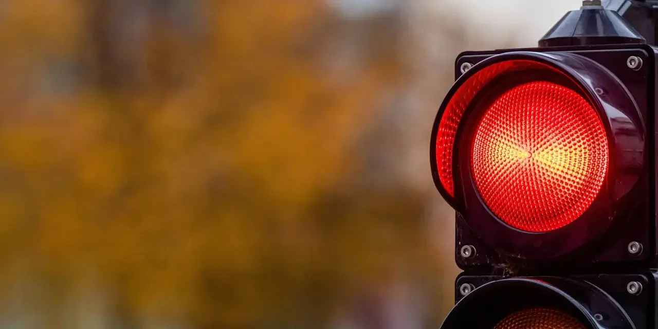 Close-up of a red traffic light with a blurred background of autumn foliage.