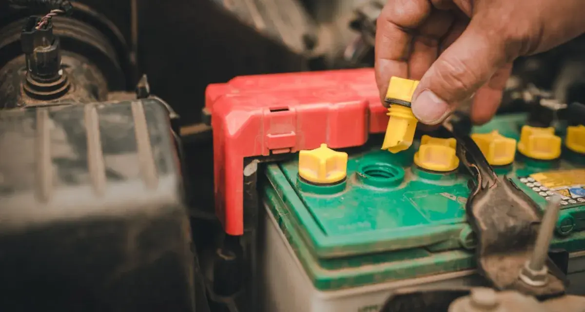 A hand removes a yellow cap from a truck battery, hinting at maintenance to ensure it lasts as long as possible.