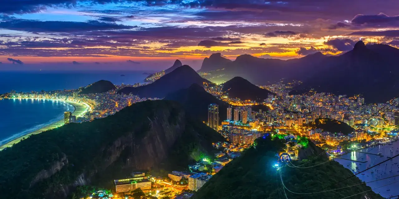 Zachód słońca nad słynną plażą w Rio de Janeiro. Miasto rozświetlone tysiącami świateł, góry i ocean tworzą magiczny widok.