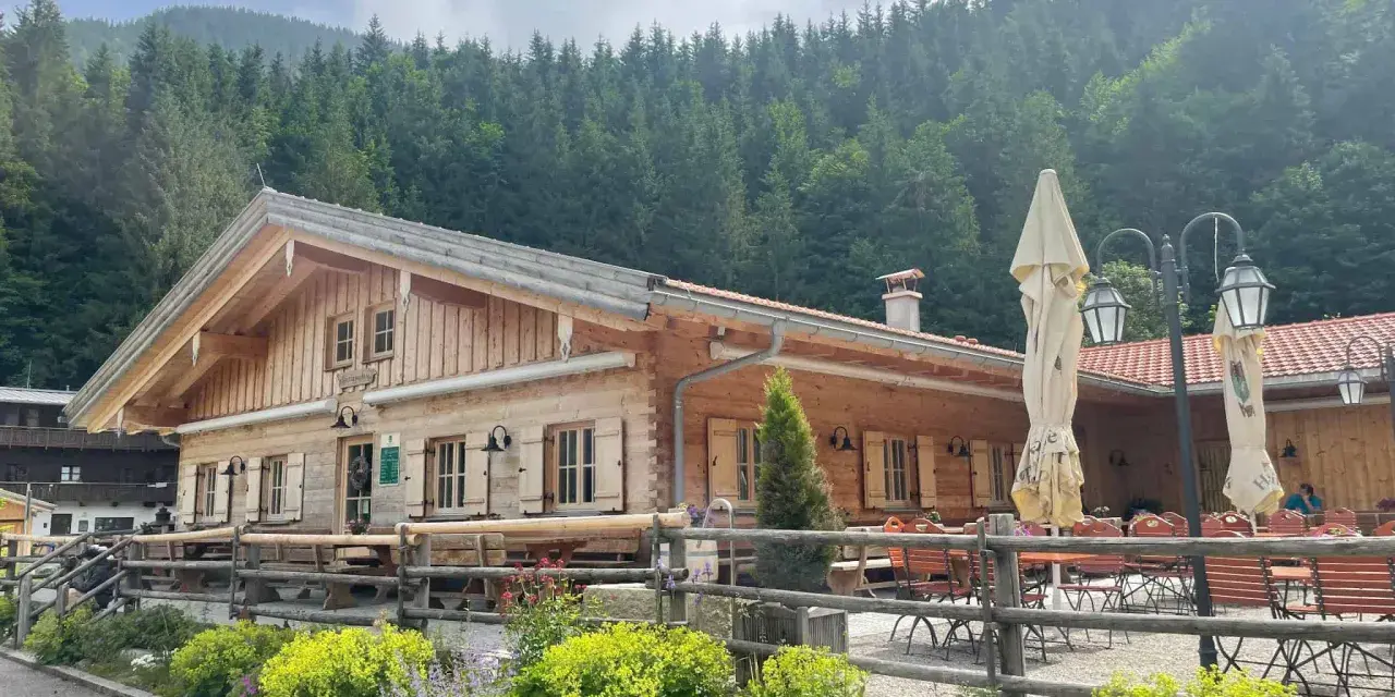 Holzhütte mit Biergarten und blühenden Blumen vor einer Bergkulisse. Die untere Firstalm lädt zum Verweilen ein.